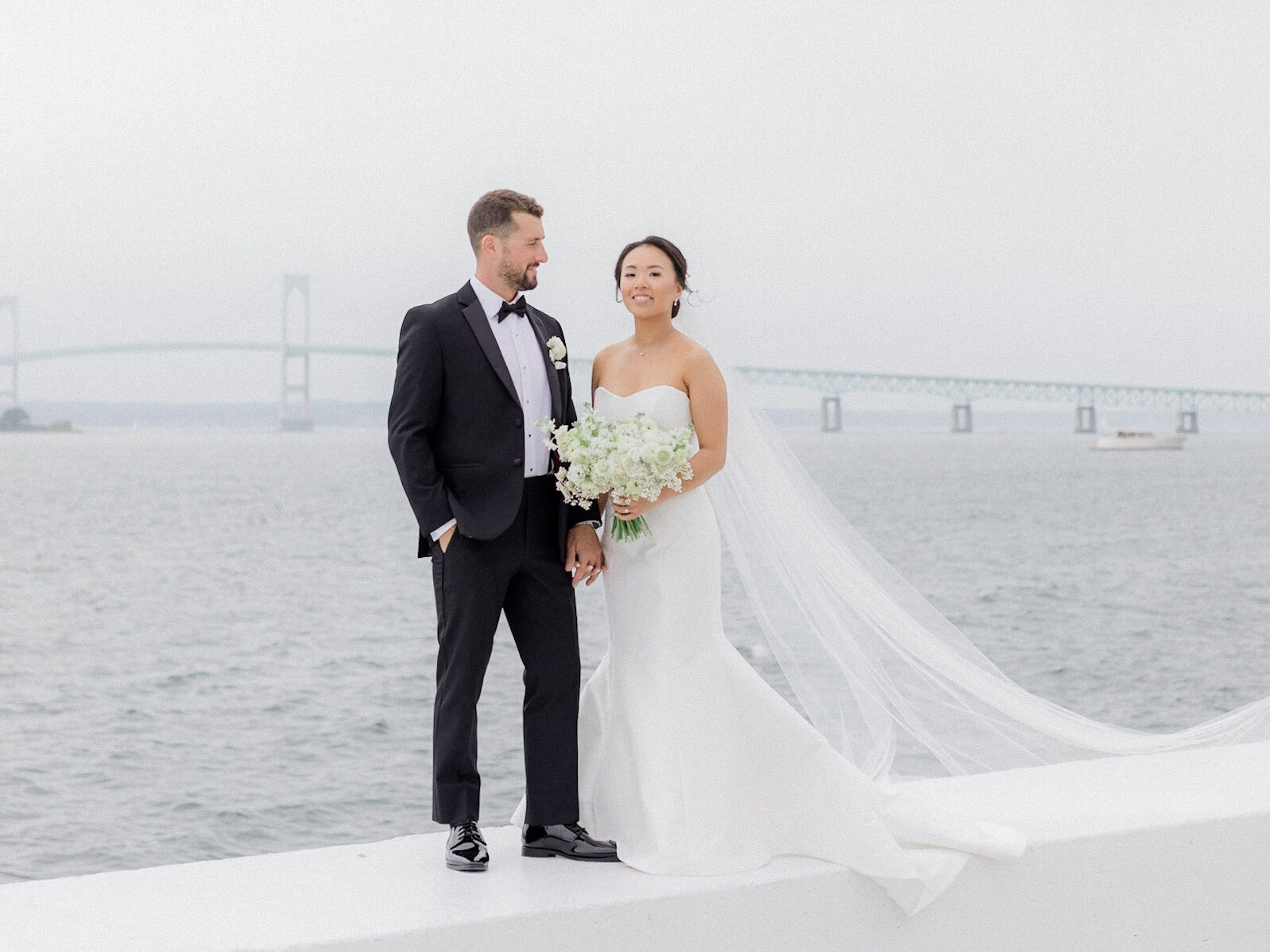 bride and groom standing on wall infront of the ocean at belle mer